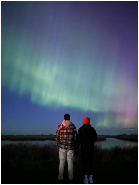 A couple stands together gazing at the aurora bore