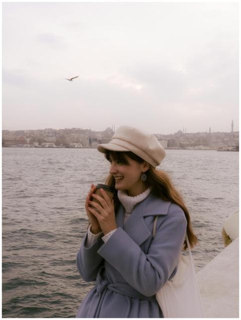 Woman in a coat and hat smiling while holding a co