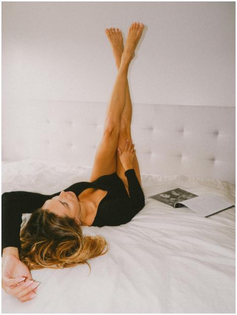 A woman in a bodysuit lies on a bed reading, legs