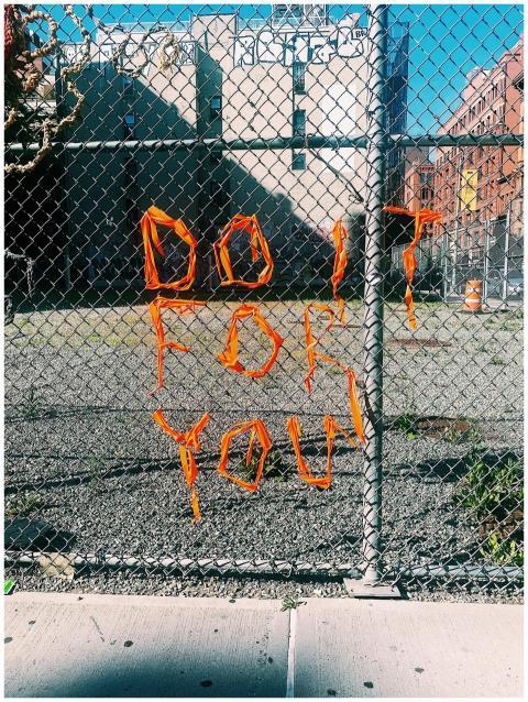 Chain link fence with orange yarn spells out 'Do I