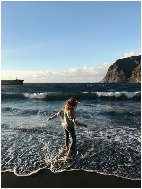 Woman stands in waves at Santiago del Teide beach,