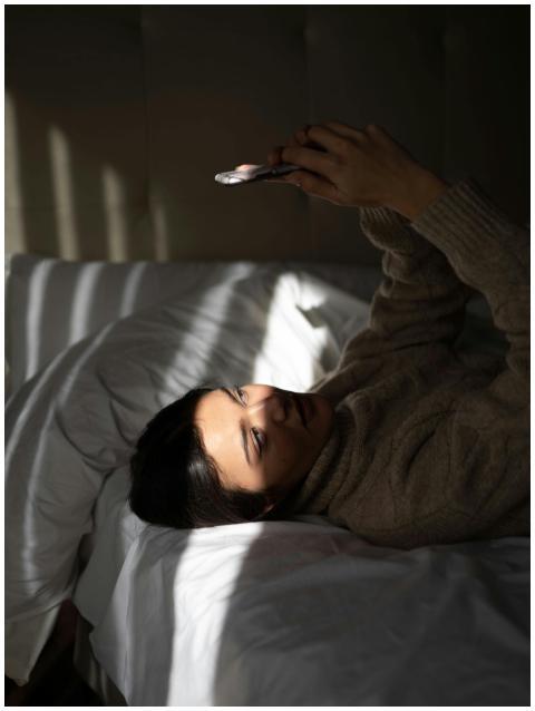 Young woman lying on bed using smartphone in brigh