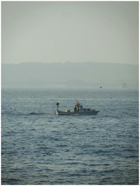 Small boat sailing on peaceful water with misty ho