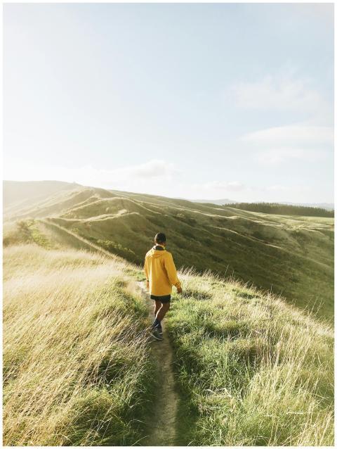 A man in a yellow jacket hikes along a grassy hill