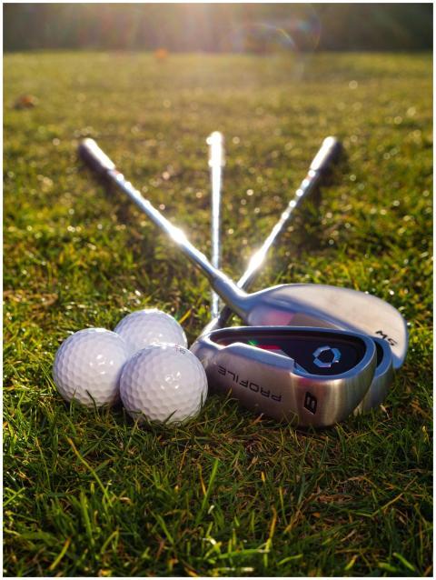 Golf clubs and balls arranged on a sunlit grass fi