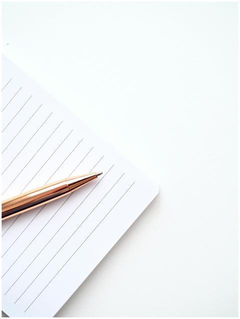 A close-up shot of a gold pen on a lined notepad w