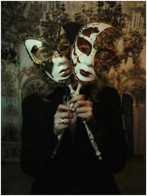 Two ornate Venetian masks held by a person in a di