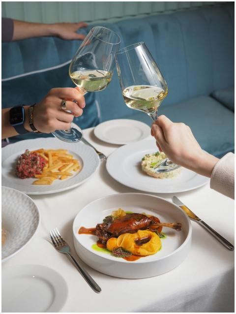 Two people toasting wine glasses over a gourmet me