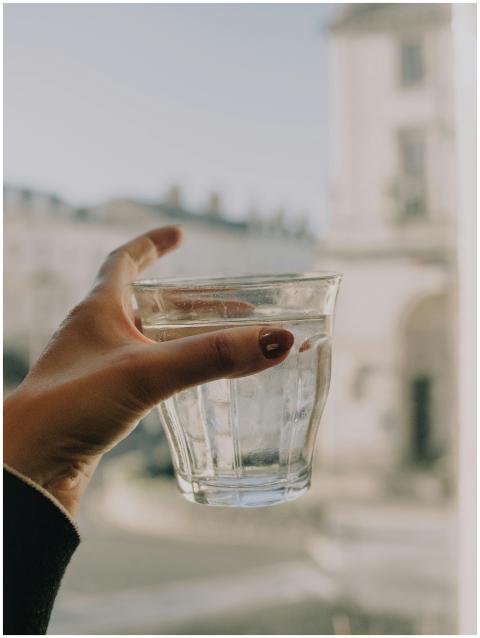 A hand holding a glass of water indoors, with a bl