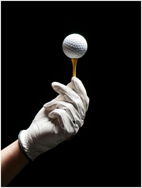 A gloved hand elegantly holds a golf ball on a tee