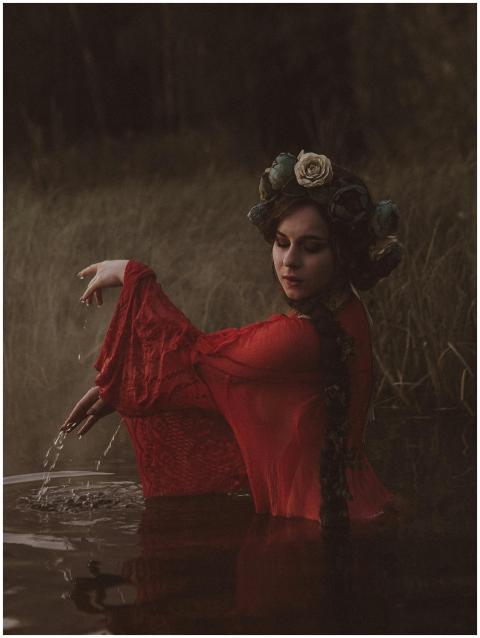 A woman in a red dress with floral headwear poses