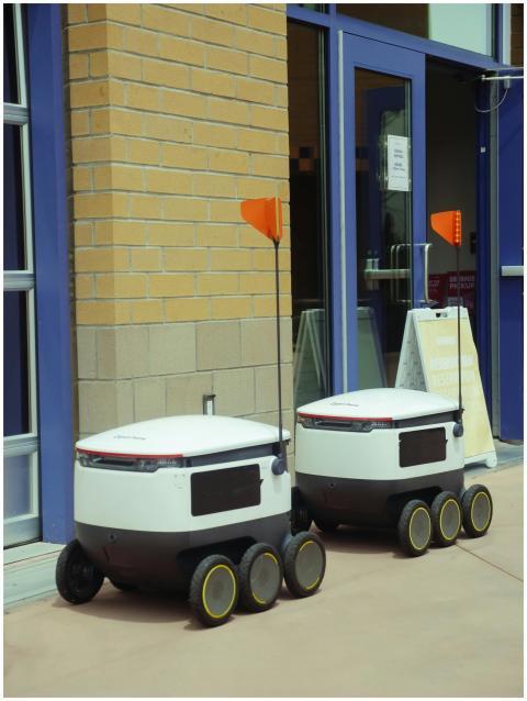 Two modern delivery robots wait outside a building