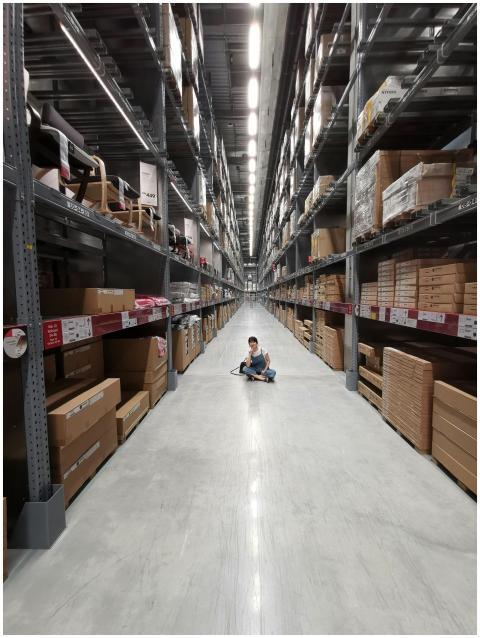 An Asian woman sits in a large warehouse aisle fil