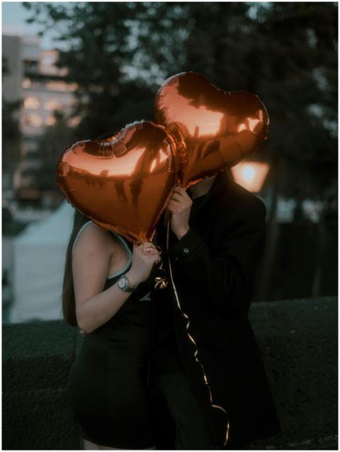 A couple holding heart-shaped balloons embracing i