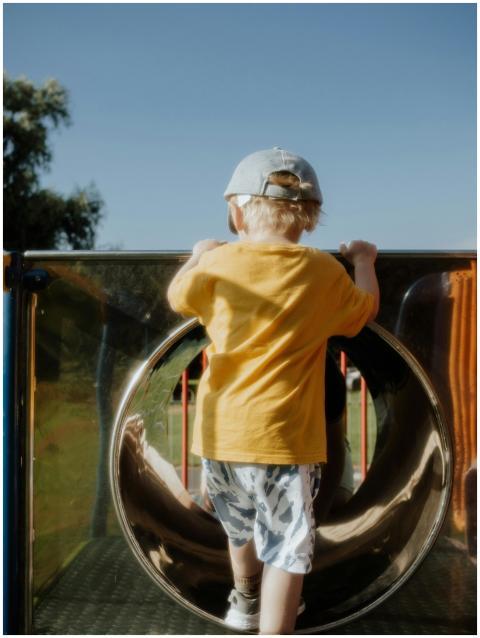 A young child climbing a playground slide on a sun