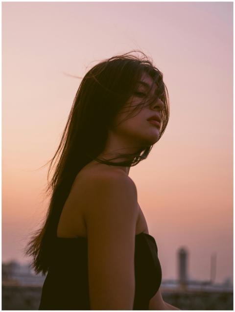 A young woman stands at sunset, hair blowing gentl