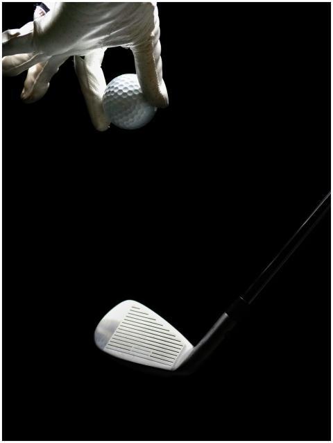 Golf ball held by a gloved hand with a golf iron a