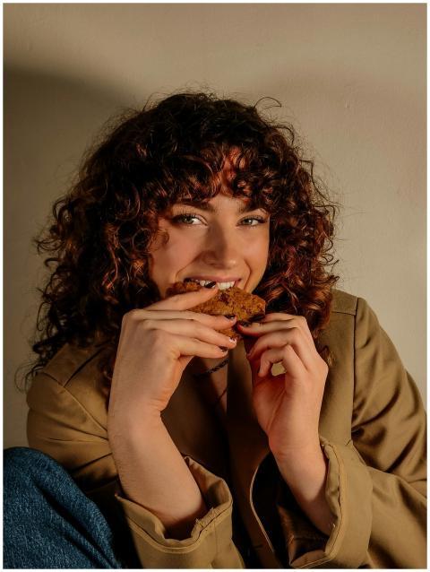 Young woman with curly hair enjoying a cookie indo