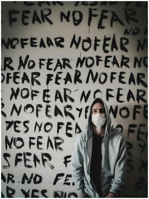 Person in a hoodie with mask stands before 'No Fea