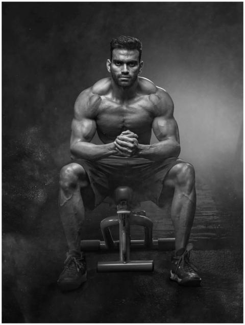 A powerful bodybuilder sitting with intense focus,