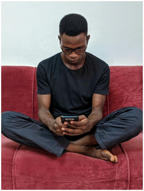 African man sitting on a red sofa indoors, using a