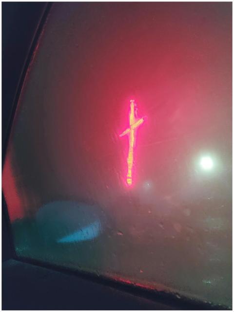 Blurred neon red cross shining through a foggy car