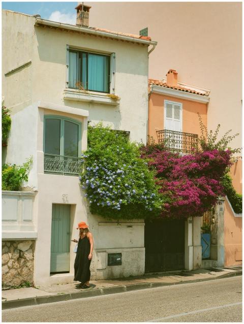 A woman in a hat walks past colorful buildings ado