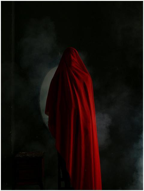 A person stands cloaked in red fabric against a sm