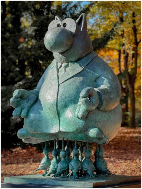 Bronze cat sculpture with birds in an autumn park