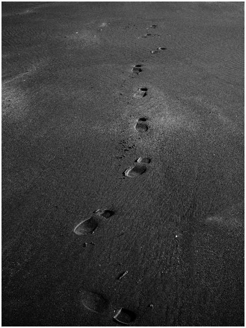 Black and white image of footsteps in sand, captur