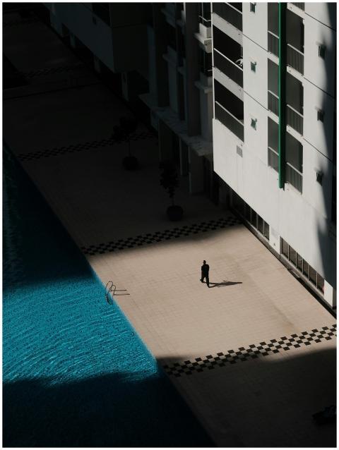 A lone figure casts a shadow by a bright blue pool