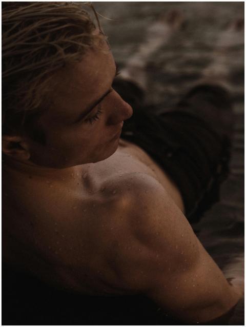 A shirtless man relaxing at the beach during dusk,