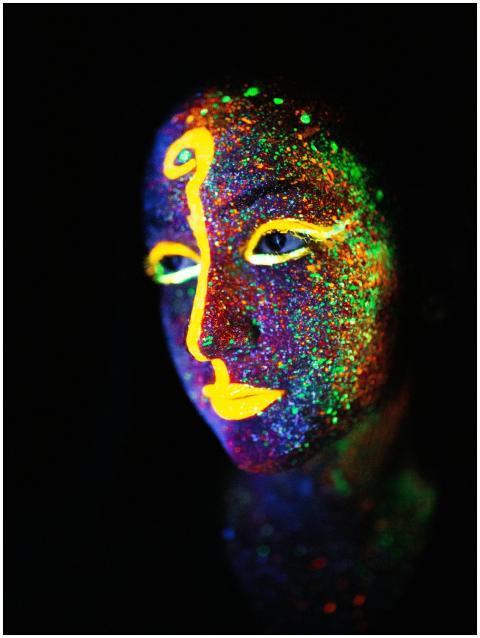 Close-up of a face painted with glowing neon color