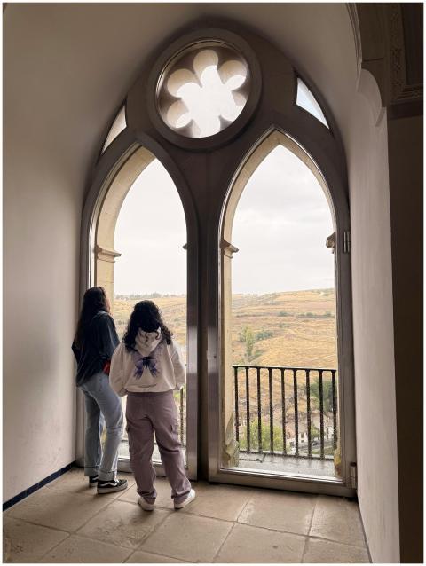Two people enjoy the view from a gothic window, sh