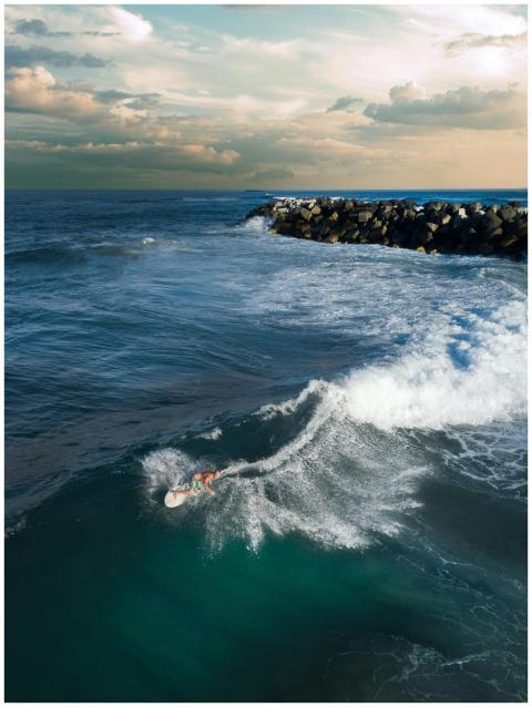 Drone shot capturing a surfer riding waves near a