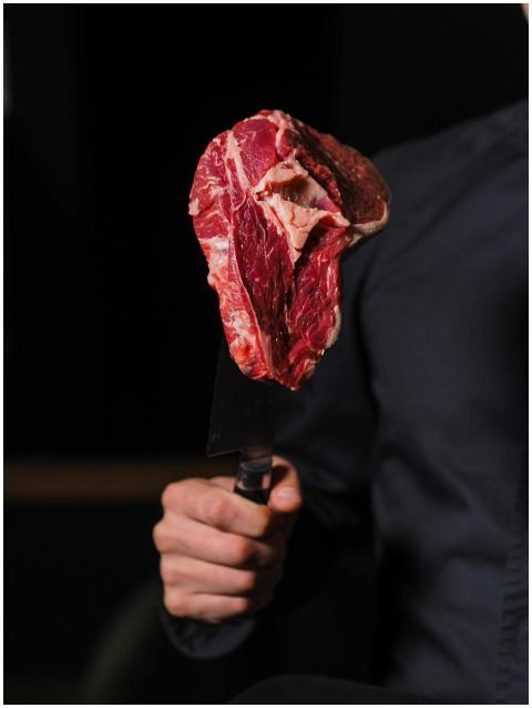 A person holds a raw steak on a knife, ready for c