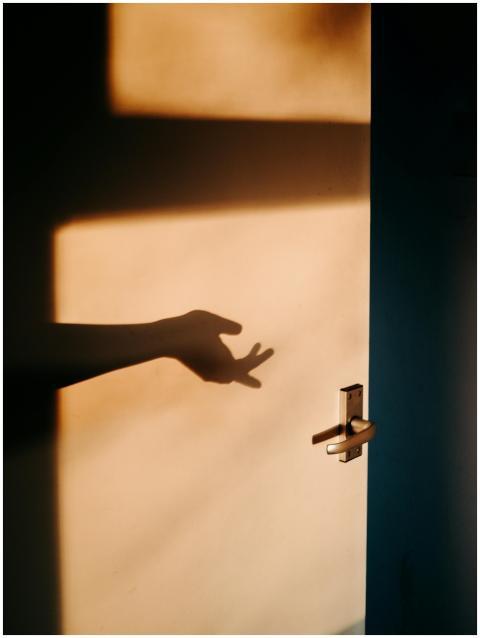 A shadow of a hand reaching on a sunlit door, crea
