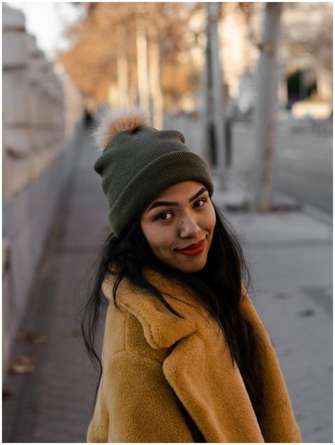 A young woman in a warm coat and beanie smiles war