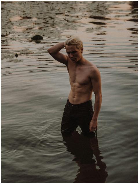 Shirtless young man standing in water during golde