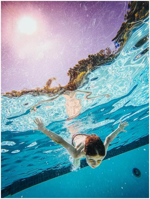 Child swimming underwater in a sunlit pool, enjoyi