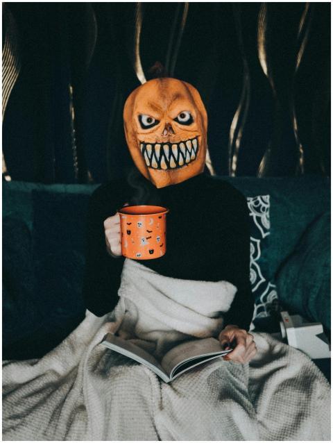 Person in pumpkin mask holding an orange cup, cozy
