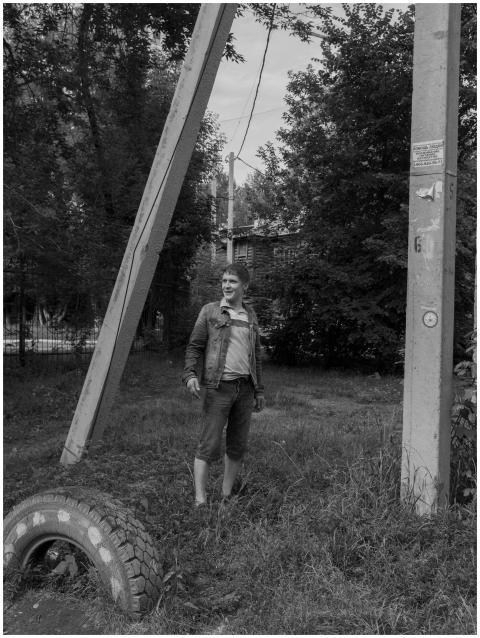 A man stands in a grassy field next to industrial
