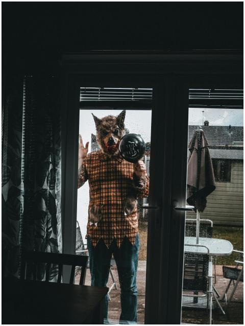 A man in a wolf mask holding a balloon stands outs