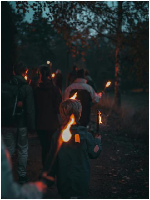 A group walks with torches through a dimly lit for