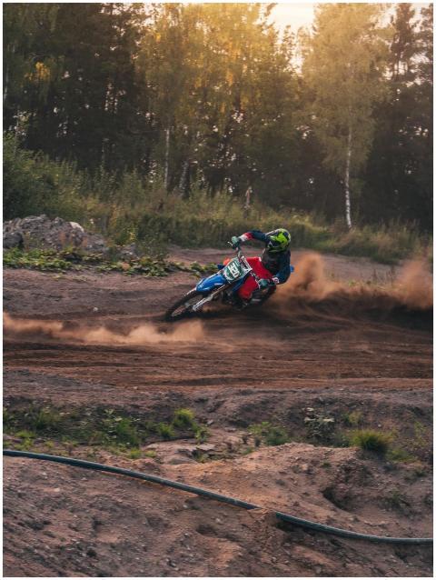 Motocross rider kicks up dust on a dirt track surr