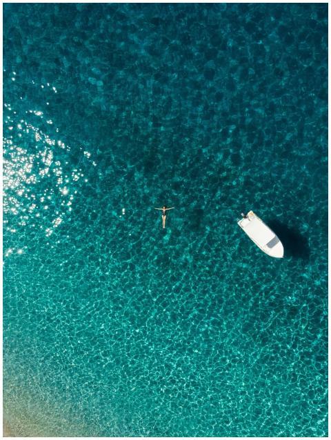 Drone shot of a woman floating in clear blue water