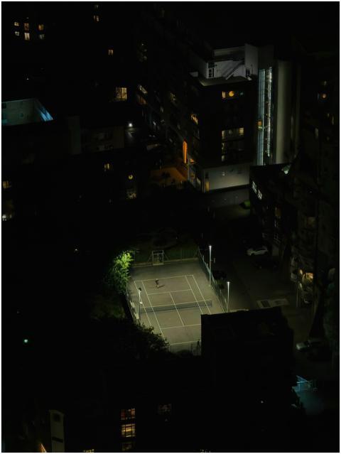 Aerial night view of a lit urban tennis court surr