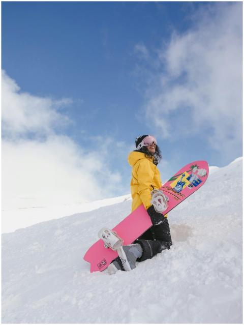 Smiling woman in winter attire with pink snowboard