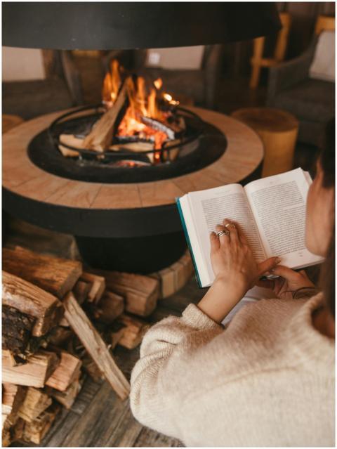Person reading by a warm indoor fireplace, enjoyin
