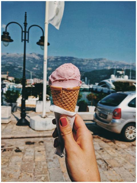 Hand holding a pink ice cream cone with a coastal